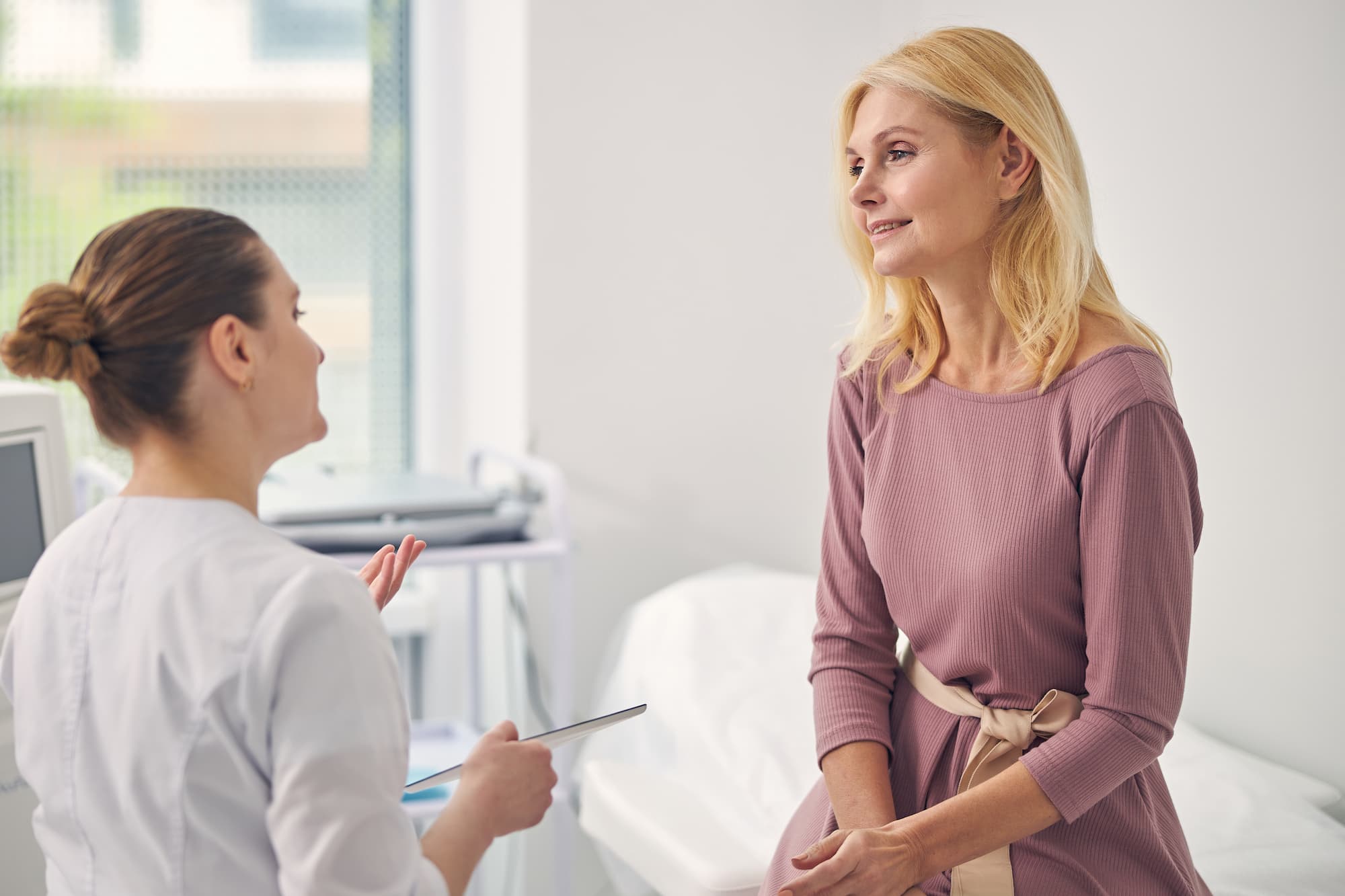 An older woman speaks with a female physician in a medical office about menopause treatment near Brookhaven.