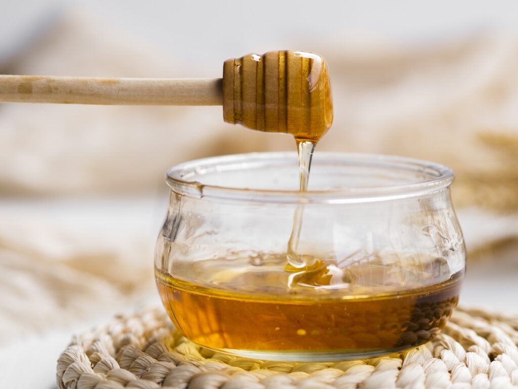 A close-up image of a honey stick scooping honey out of a bowl. Wellnest MD providers recommend honey and tea for sore throat remedies.